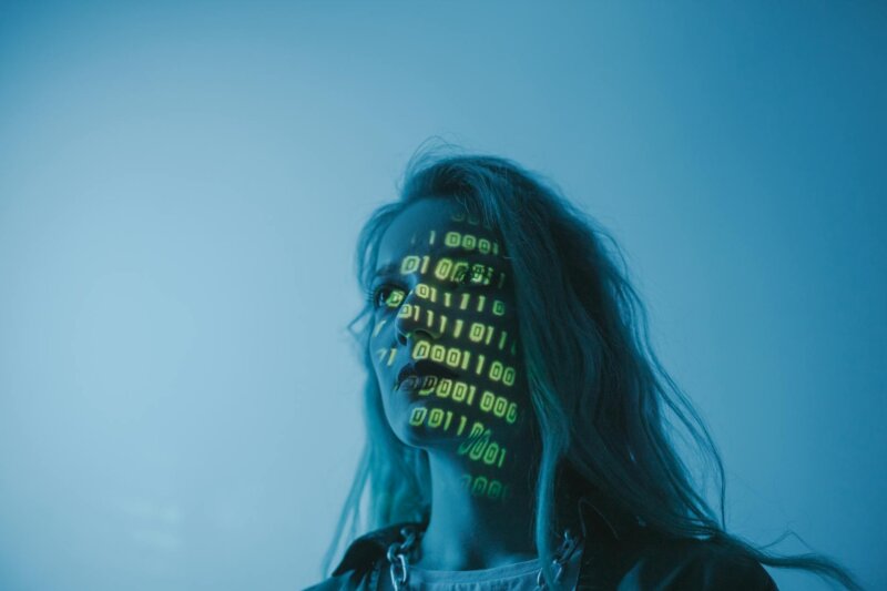 A woman with binary code lights projected on her face, symbolizing technology.