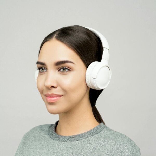 Smiling woman enjoying music with white headphones indoors, modern lifestyle portrait.