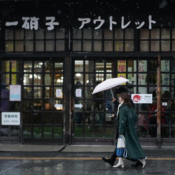 A woman walks with an umbrella in front of a traditional Japanese shop on a snowy day.