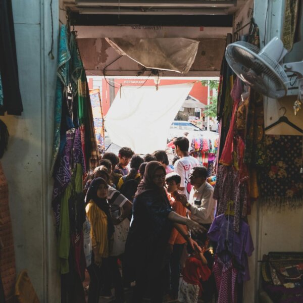 Crowded market entrance showcasing vibrant clothing, bustling with diverse shoppers.