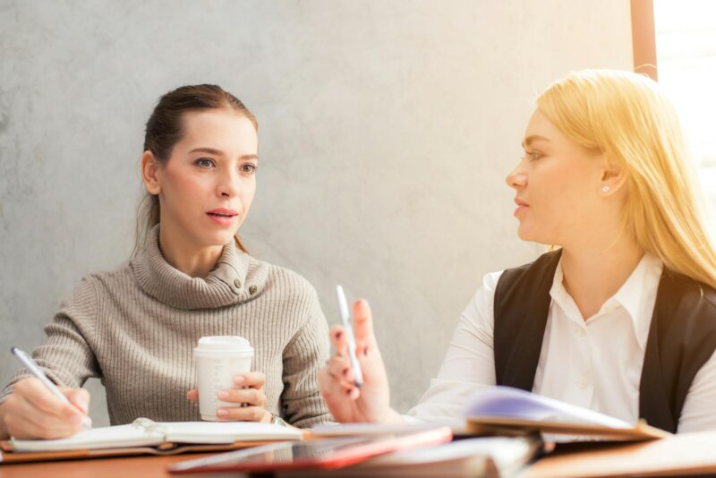 Two women engaging in a professional conversation over coffee and notes.