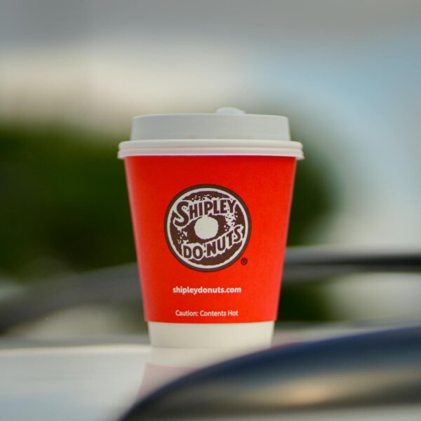 Close-up of a red Shipley Donuts coffee cup outdoors with blurred background.