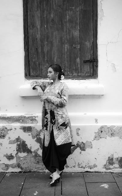Black and white photo of a woman in traditional clothing leaning against an old wall.
