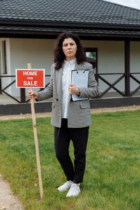 Female real estate agent outside house for sale holding sign.